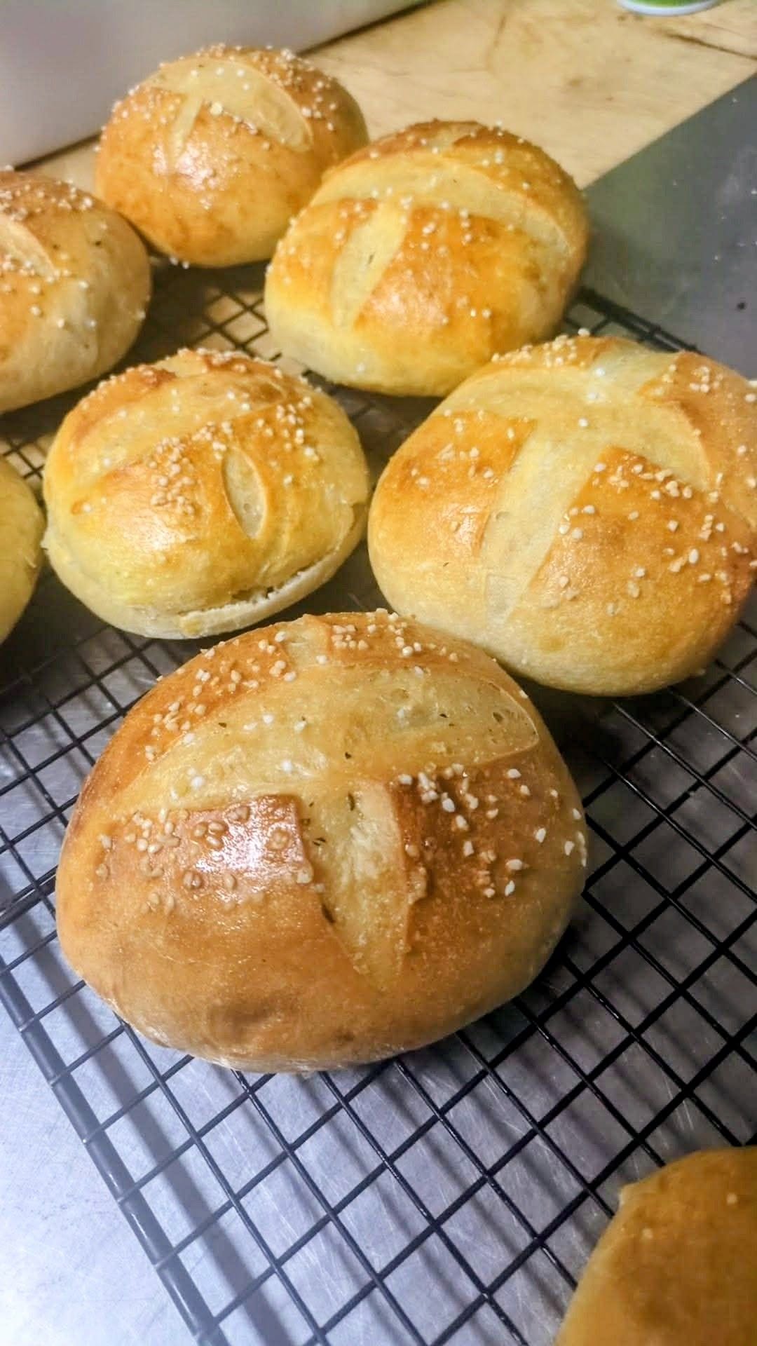 Scored pretzel buns with sesame seeds on a cooling rack